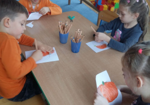 Dzieci przy stoliku robią dyniowe opaski